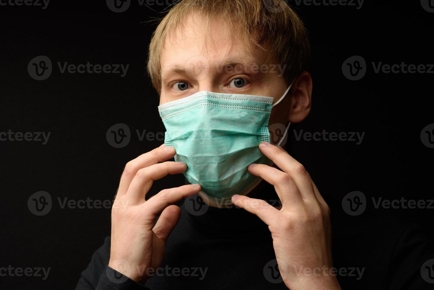 mujer joven con mascarilla médica que protege del virus. mujer seria con ojos tristes tocando máscara de protección contra la peligrosa epidemia de coronavirus y mirando la cámara sobre fondo negro foto