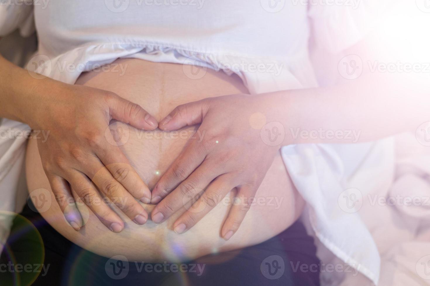 The expectant mother puts her hands on her belly to communicate with her unborn child and wait for the day when her baby is born. Concept of communication from pregnant mother to unborn child. photo