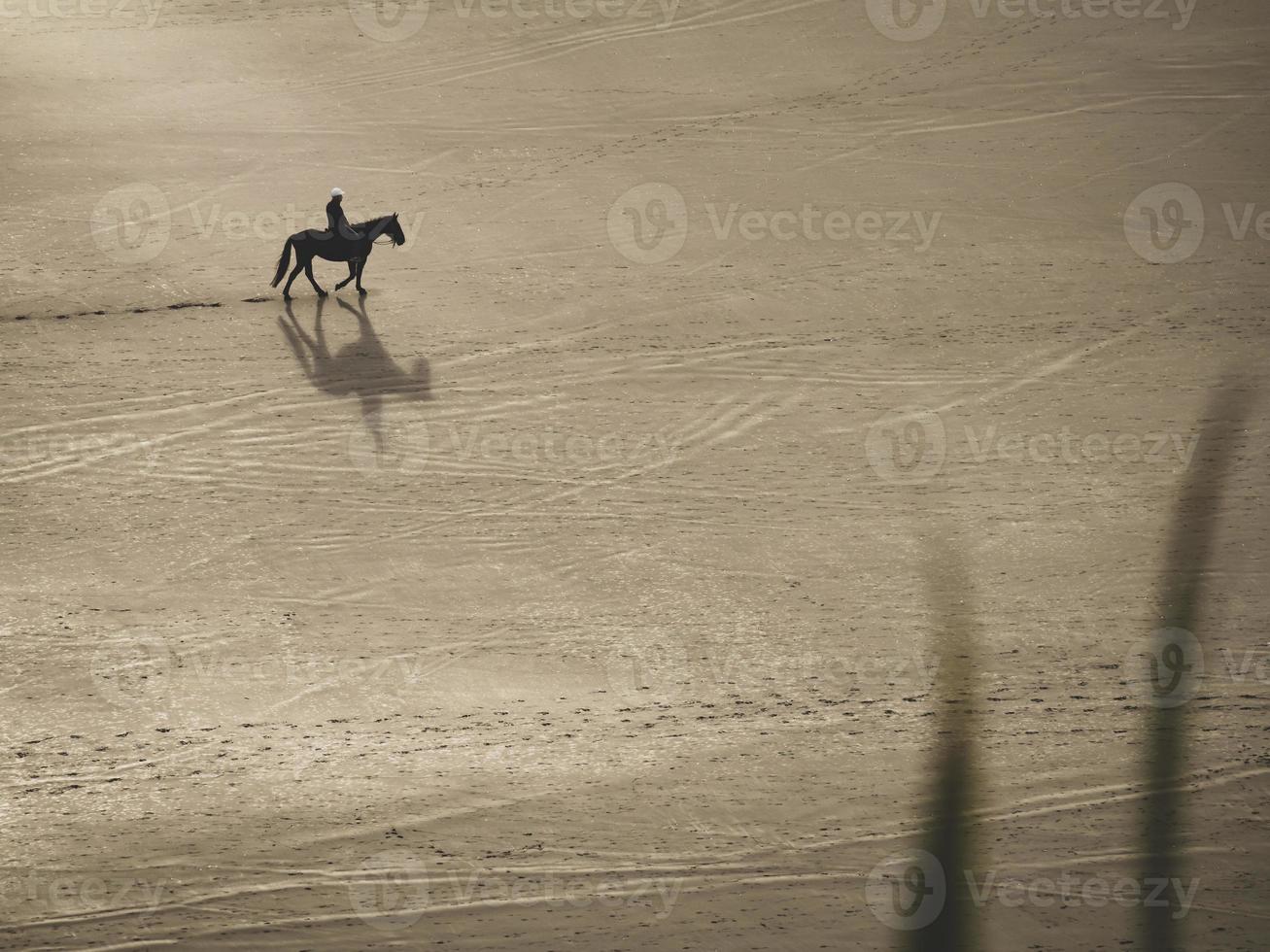 hombre montando a caballo solo en la arena a lo largo de la playa de raglan nueva zelanda con una silueta y una sombra foto