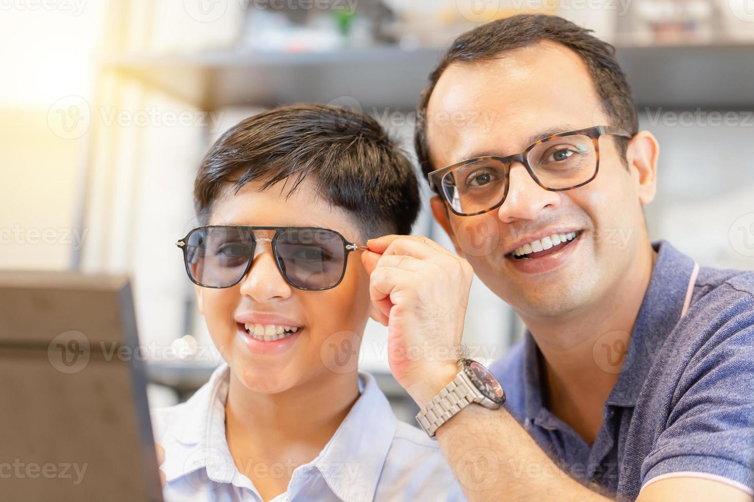 Indian kid and father choosing eyeglasses in optical store, father and son choosing eyeglasses frame in optics shop photo