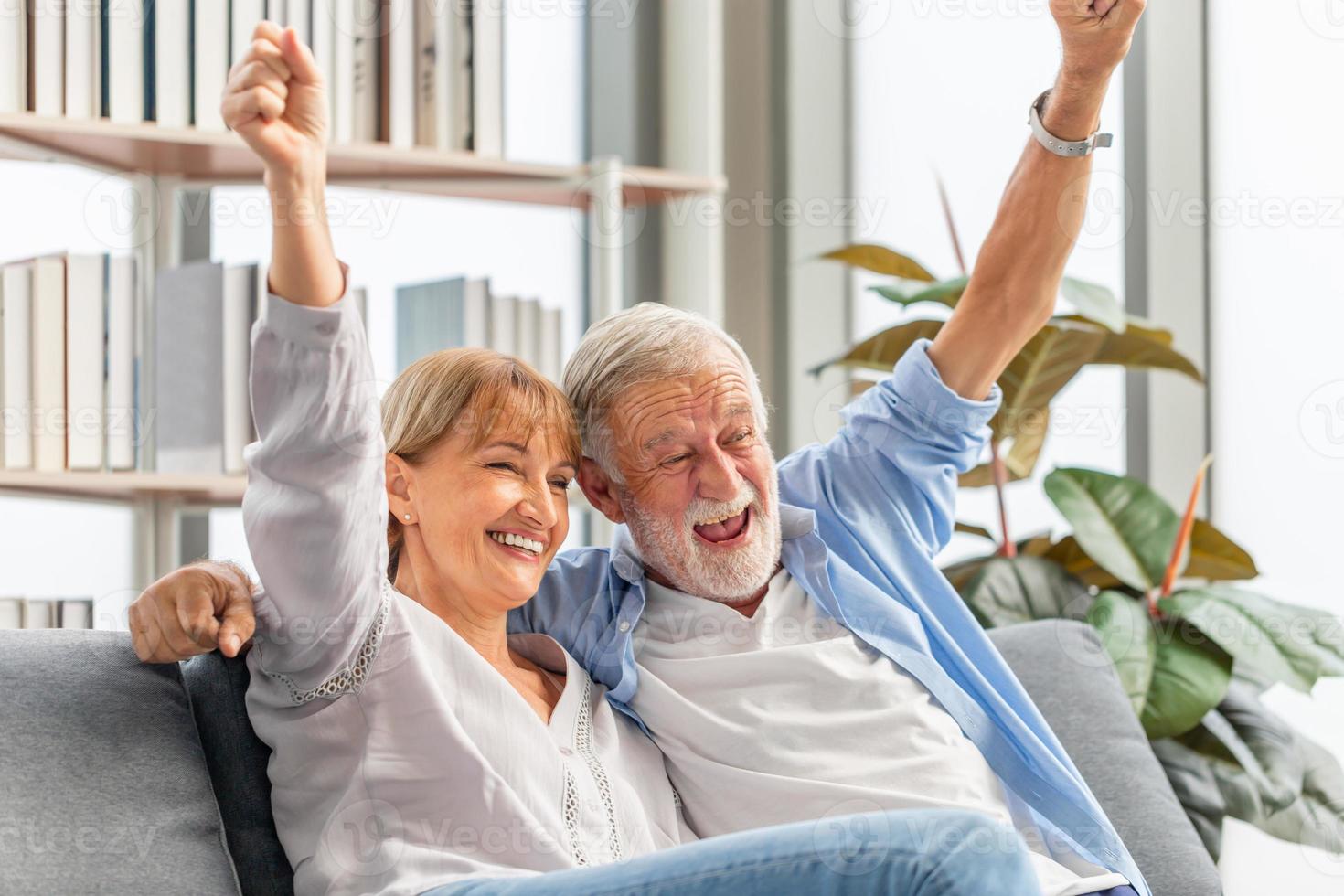 retrato de una feliz pareja mayor animando a su equipo favorito mientras ve un partido de fútbol en la sala de estar, una anciana y un hombre relajándose en un cómodo sofá en casa, conceptos familiares felices foto