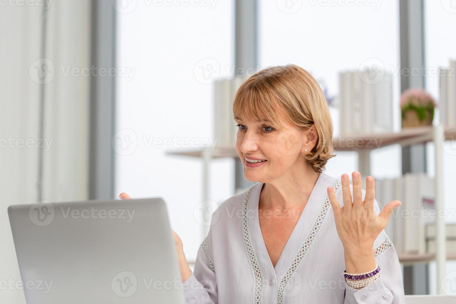 retrato de una mujer que usa una computadora portátil y un teléfono inteligente en casa, una mujer madura en la sala de estar con una videollamada hablando con una computadora portátil en un dispositivo informático moderno foto