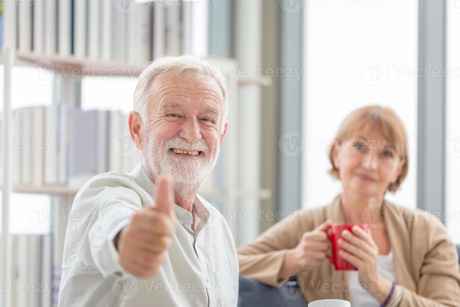 Senior couple inside home during a coffee break, Smiling elderly man showing thumbs up with holding cups of coffee photo