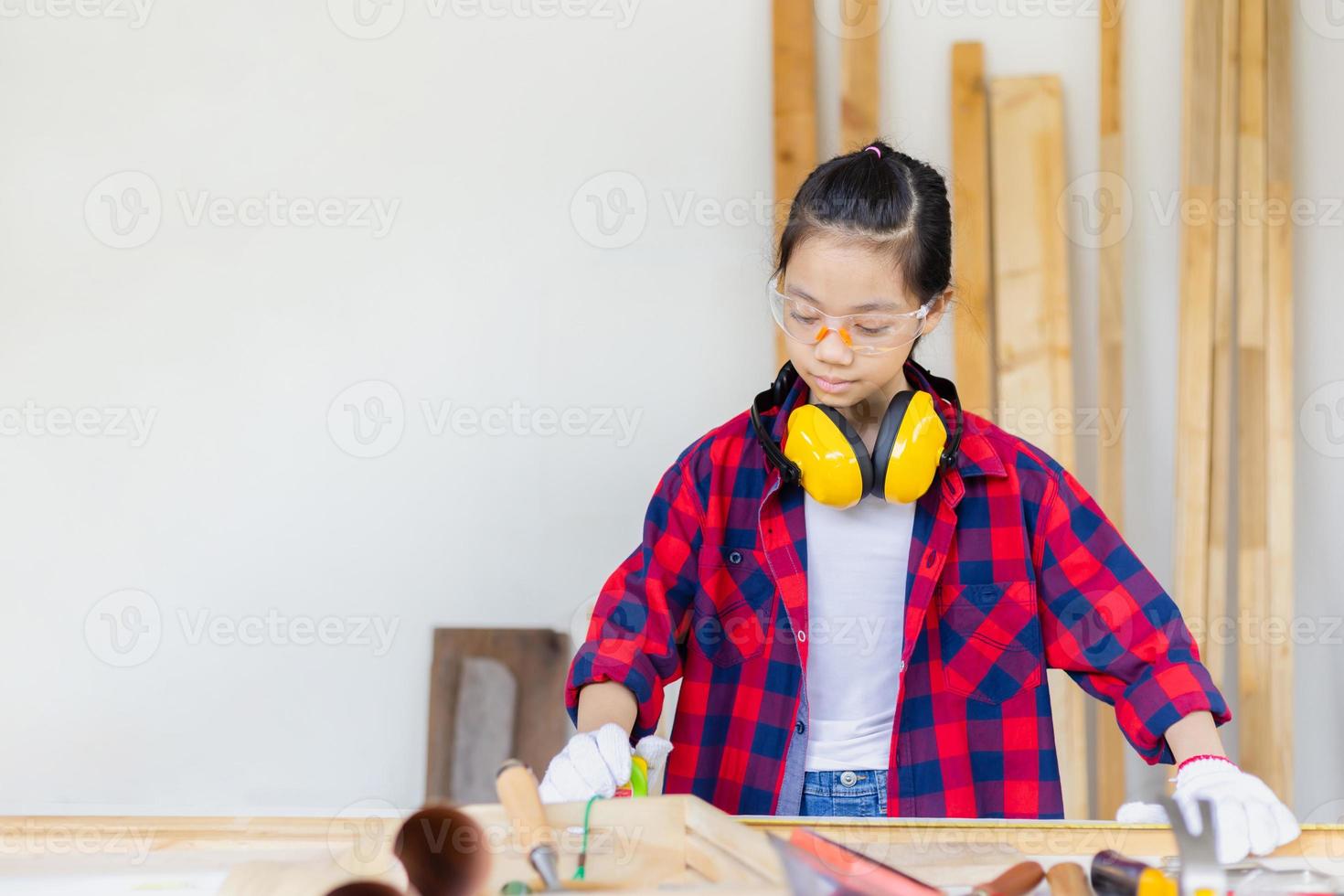 Kid learning woodworking in the craftsman workshop, Asian girl standing with noise reduction earmuffs in a carpentry workshop photo