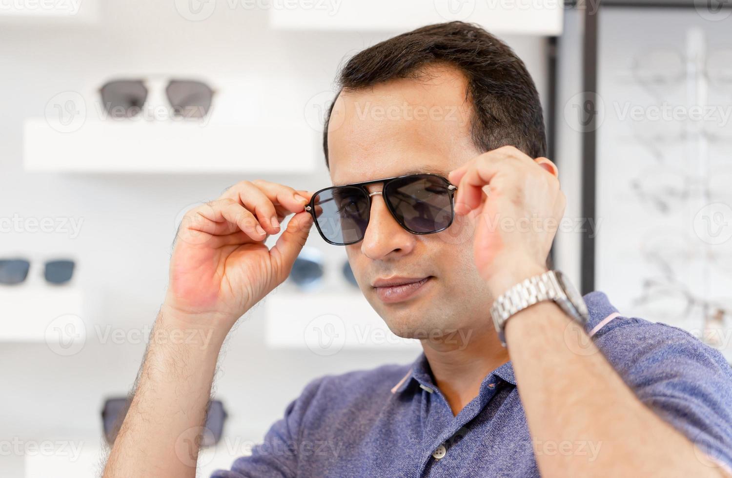 retrato de un hombre guapo con gafas de sol en una tienda de óptica, un hombre indio eligiendo gafas de sol en una tienda de óptica foto