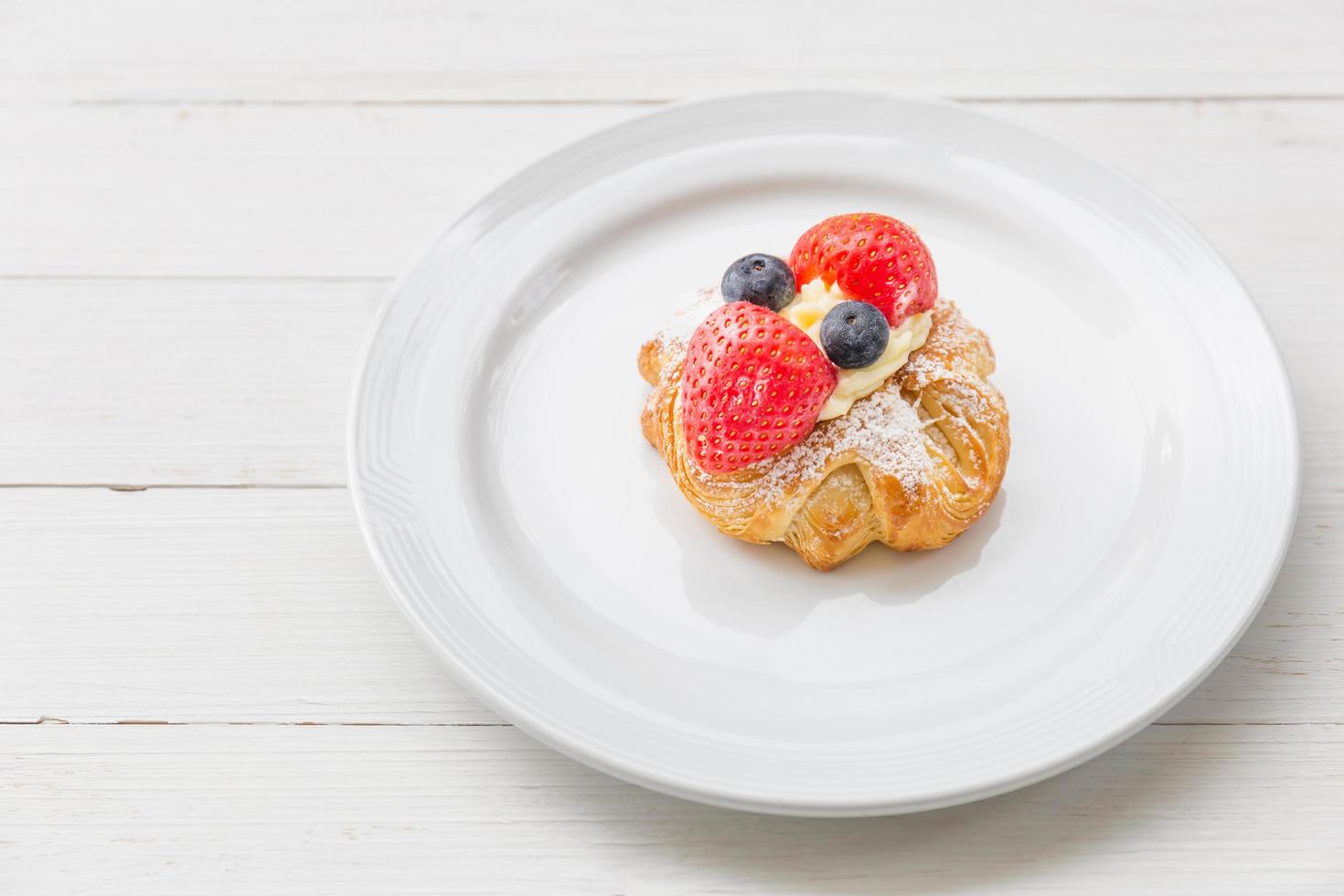 Fresh croissant with whipped cream and strawberries blueberries on a white plate photo