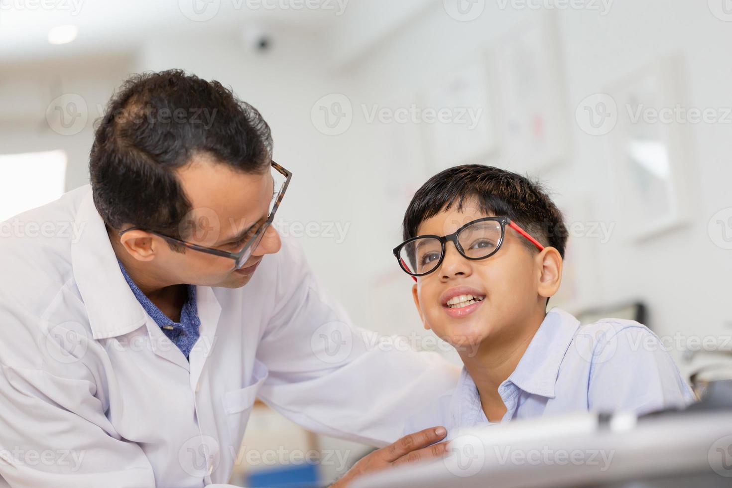 Indian child choosing eyeglasses in optics store, Boy doing eye test checking examination with optometrist in optical shop, Optometrist doing sight testing for child patient in clinic photo