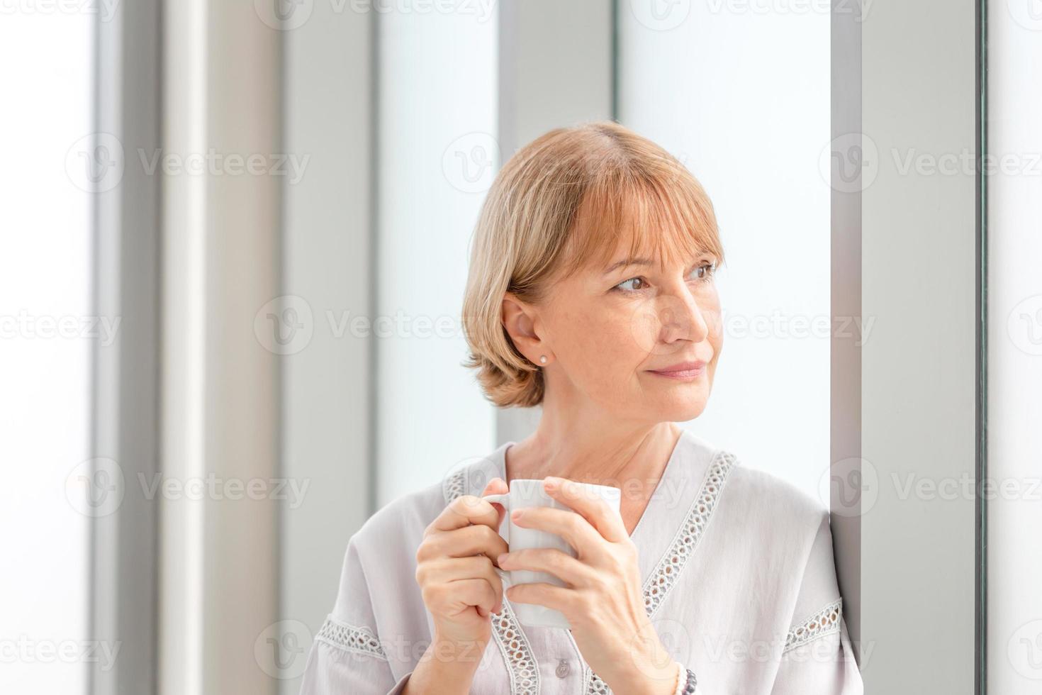 Portrait of Relaxing woman inside new home during a coffee break, Woman standing near window with cups of coffee photo