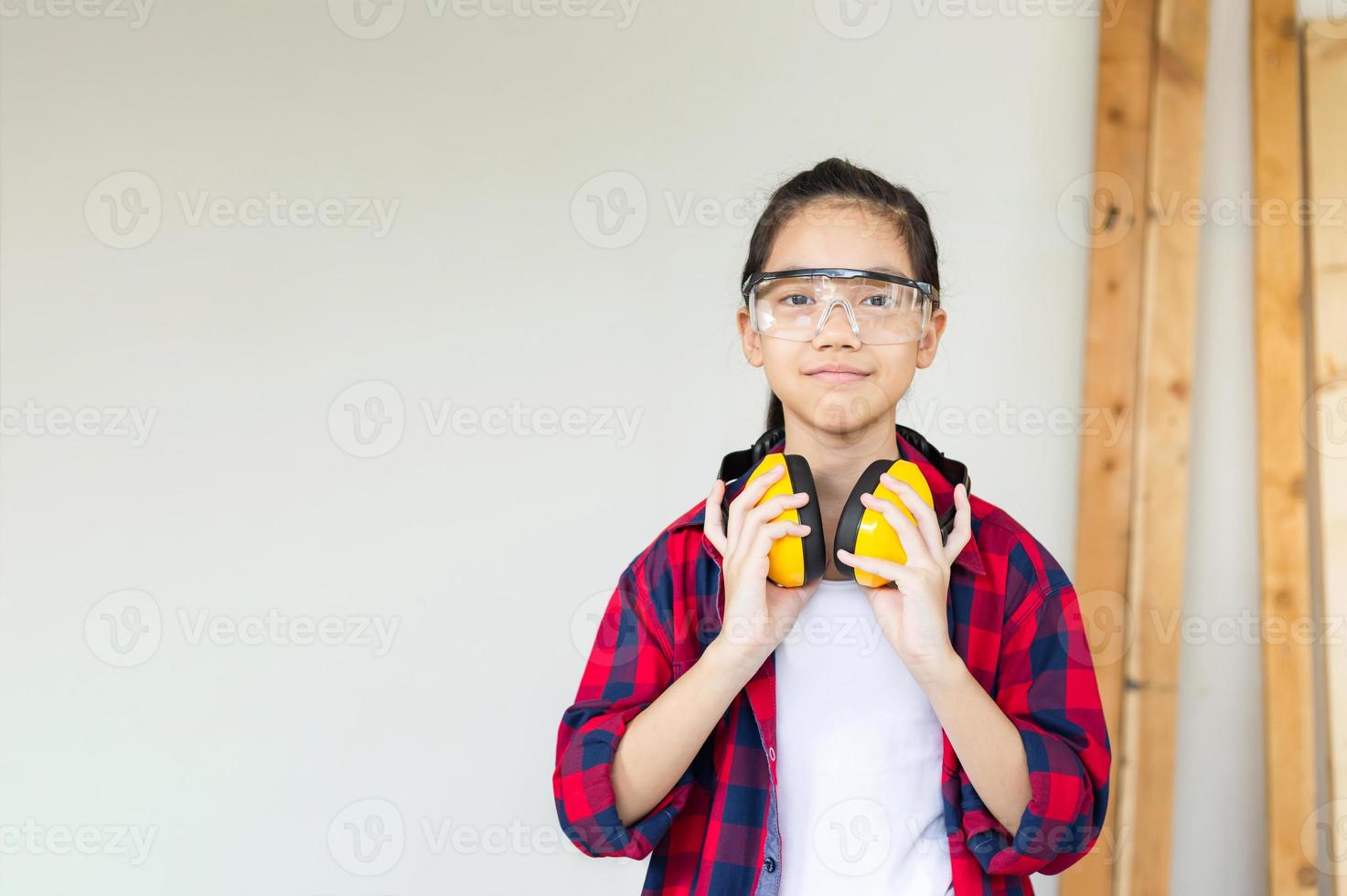 Happy girl standing with noise reduction earmuffs in a carpentry workshop. Children learning woodworking in the craftsman workshop photo