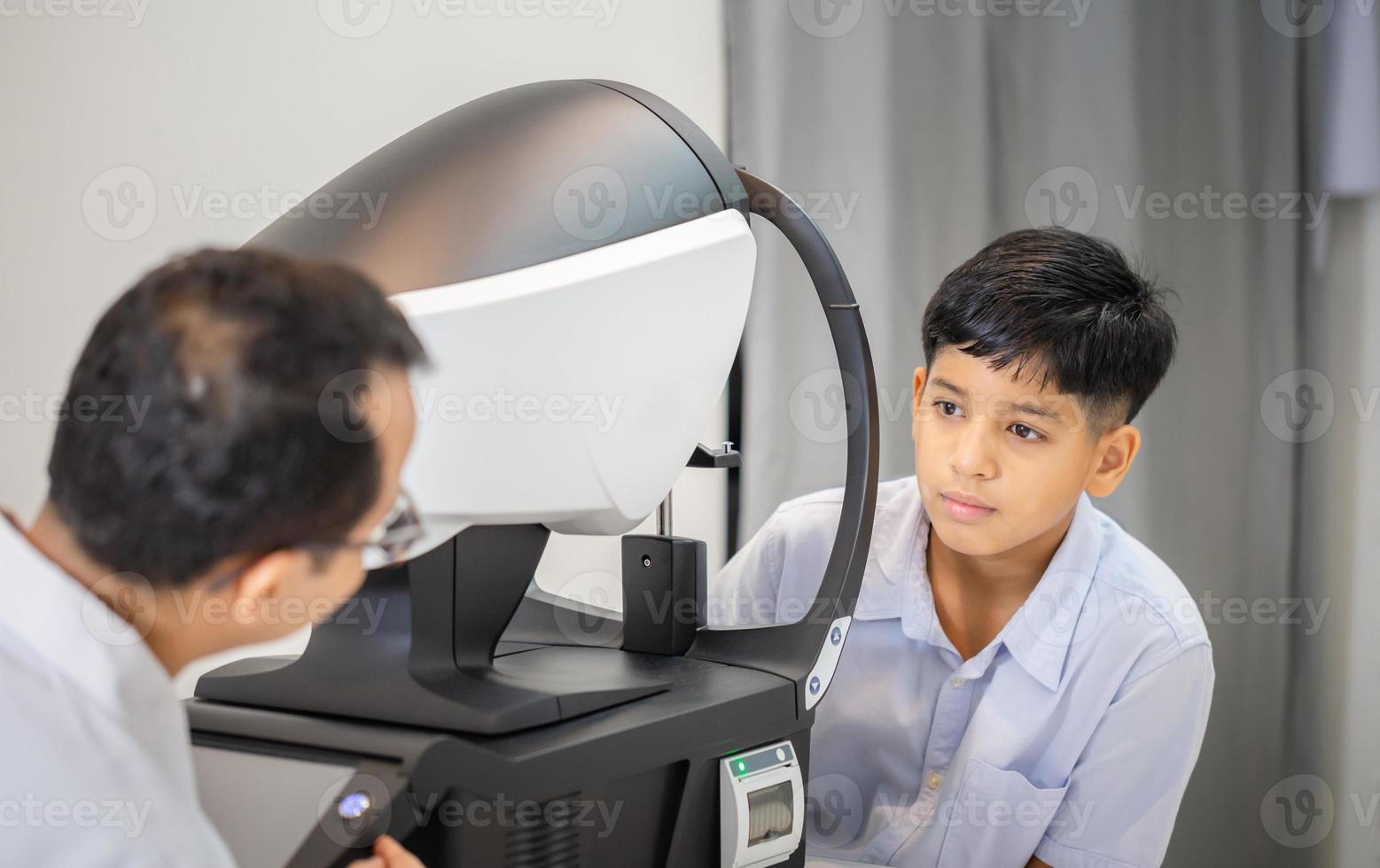 Boy doing eye test checking examination with autorefractor in optical shop, Optometrist doing sight testing for child patient, Eye doctor examinating kid patient photo