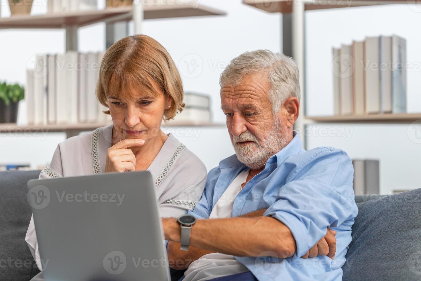 Worried senior couple checking their bills and work on netbook read document information at home, retired elderly old family reading documents with laptop photo