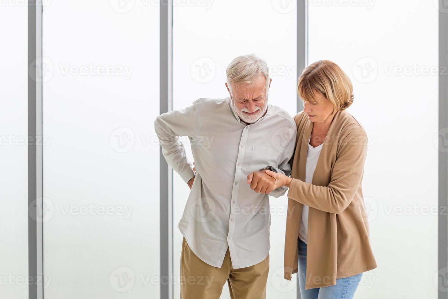 Senior man is having back pain and his attractive old woman supports him. Elderly man suffering from back pain and takes care by his wife photo