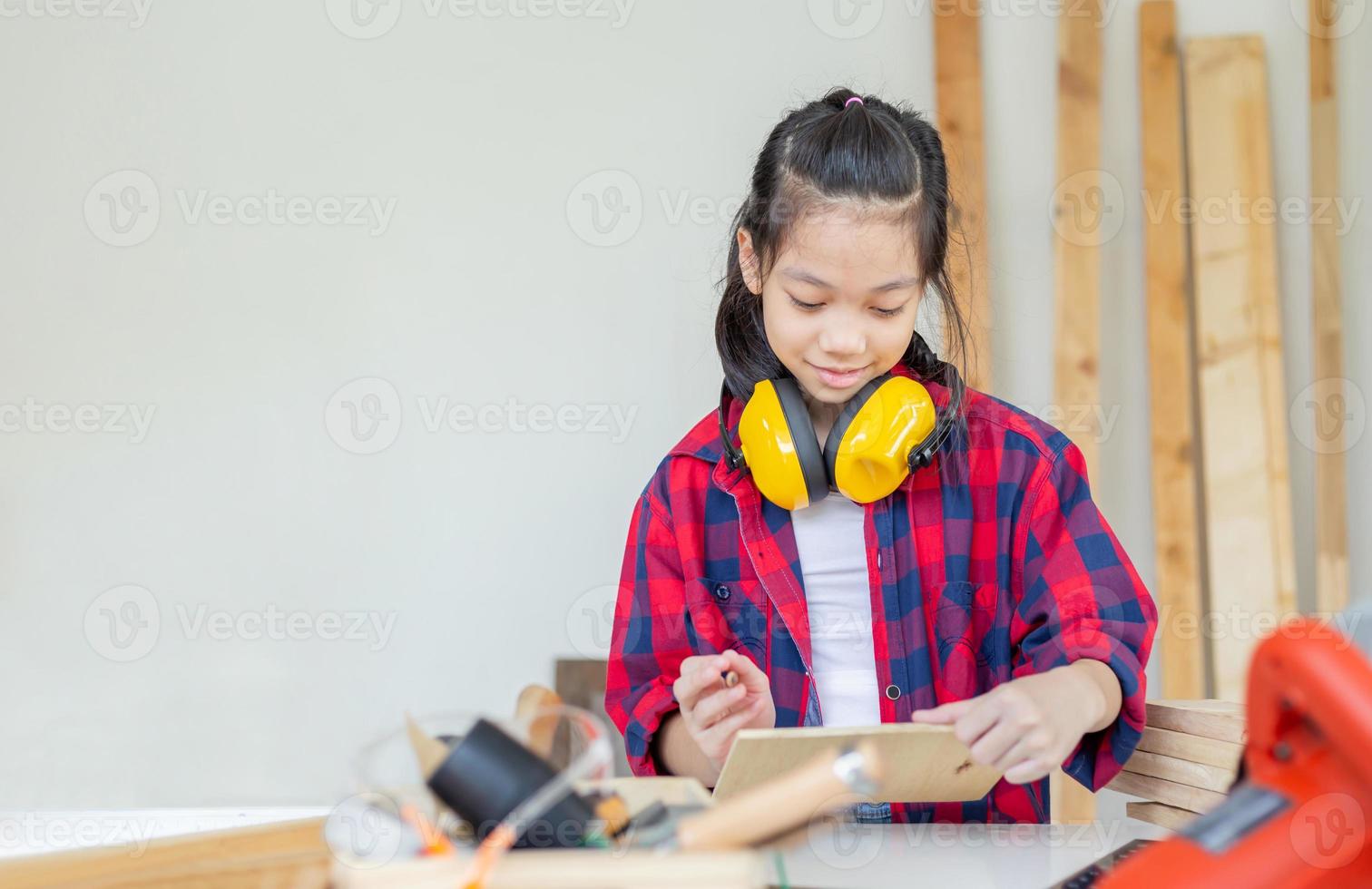 Happy girl standing with noise reduction earmuffs in a carpentry workshop. Children learning in the craftsman workshop photo