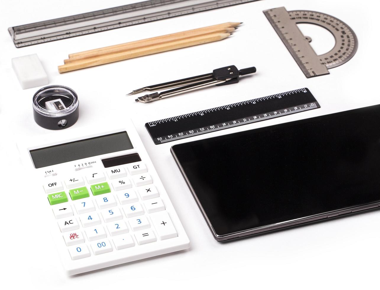 tableta, calculadora, regla, lápiz y brújula sobre fondo blanco. foto