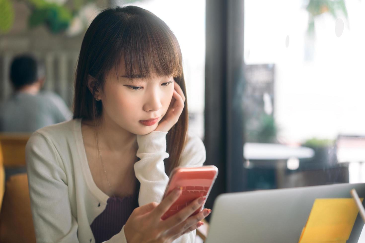 joven estudiante asiática adulta que usa un teléfono móvil para una aplicación en línea en un café interior. foto