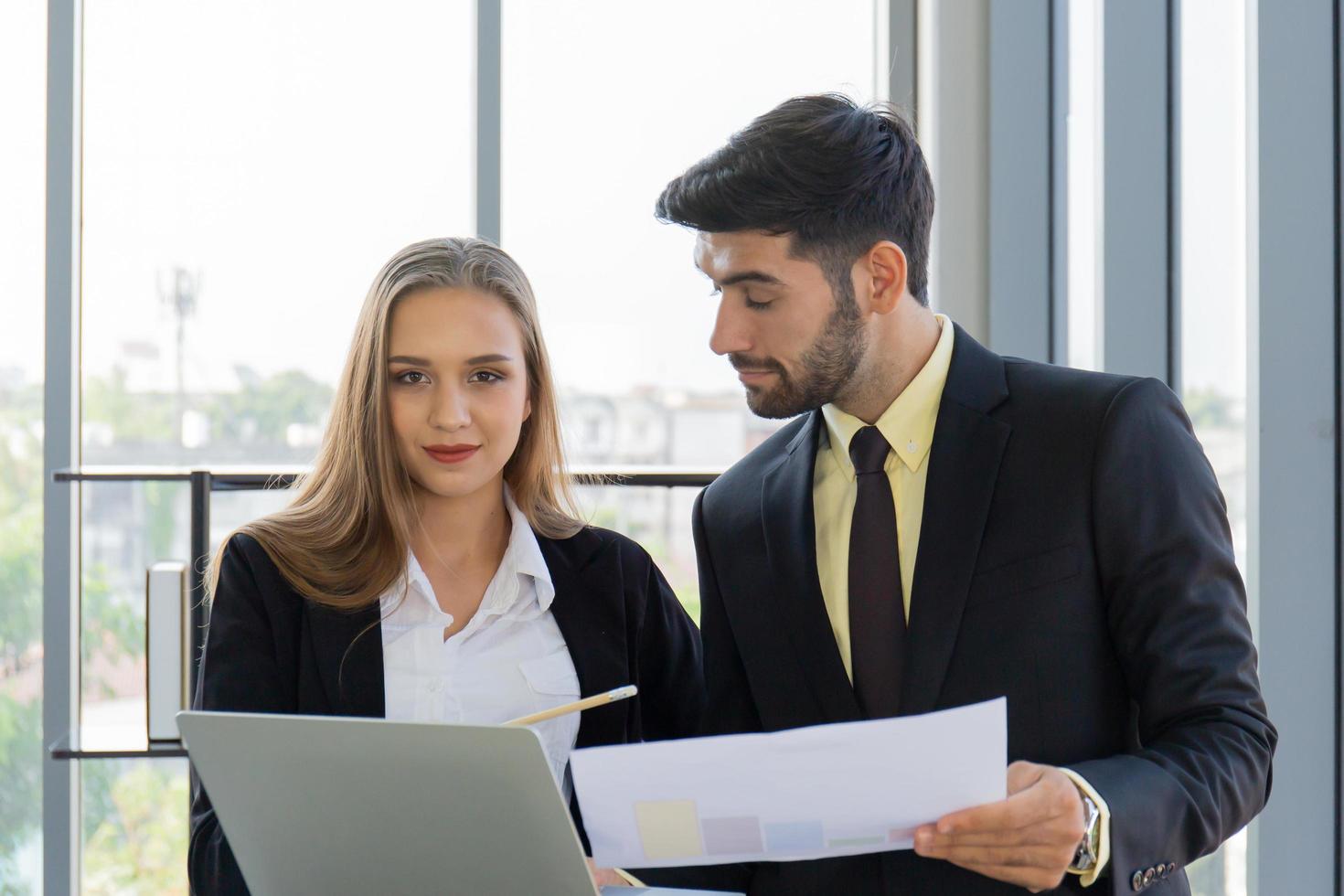 Two business men and women were neatly dressed in a suit and tie standing meeting beside the glass wall in the office. photo