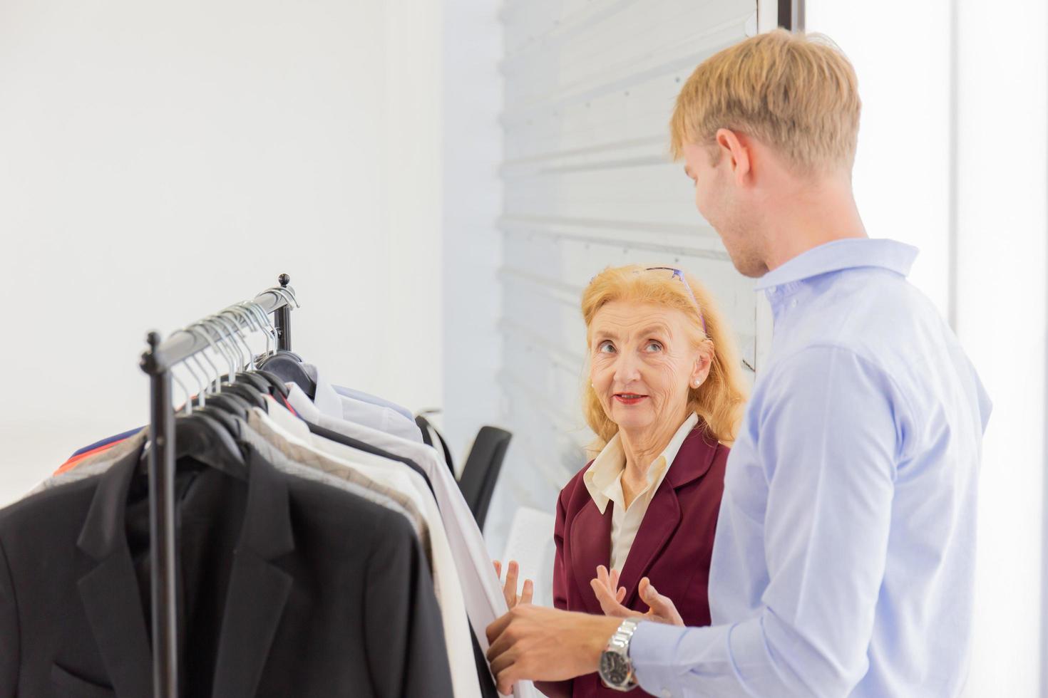 An elderly female designer is explaining information to customers about male suits. photo