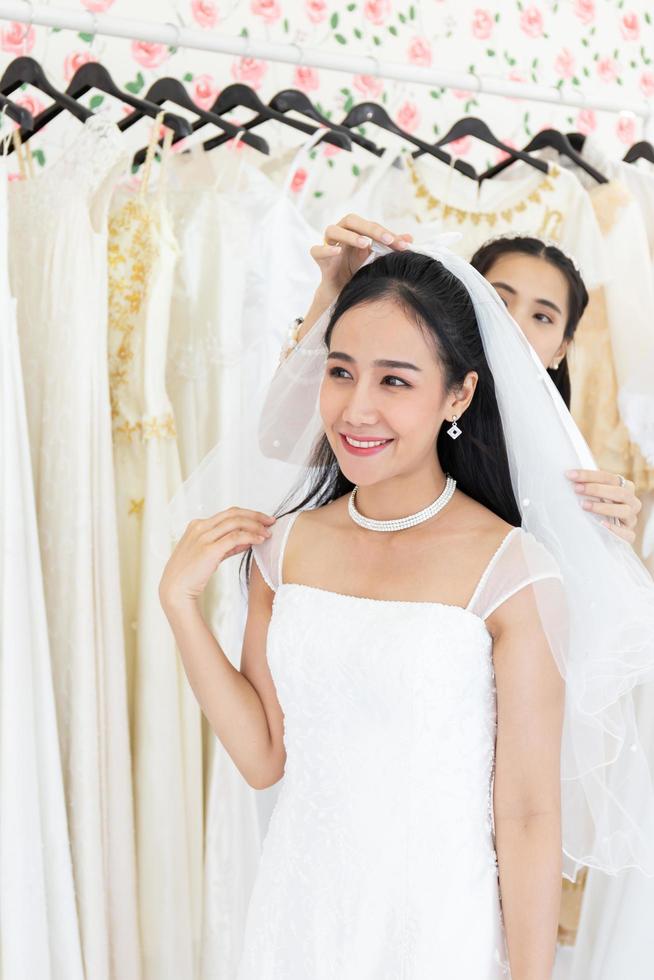 An Asian bride in a white wedding dress is trying her upcoming wedding dress in the fitting room. photo