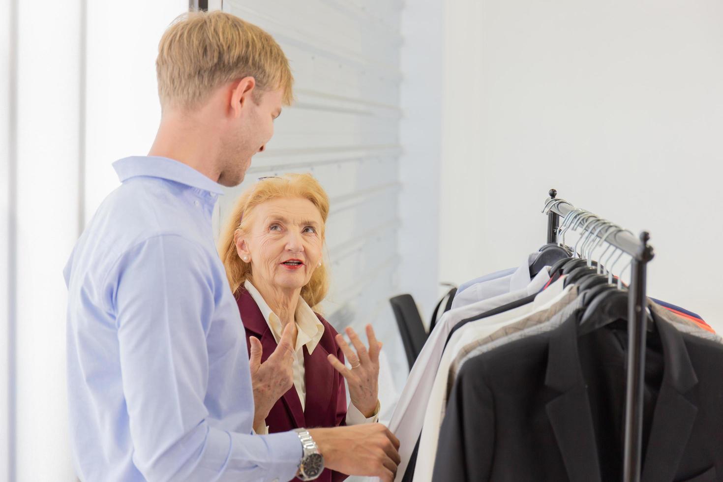 An elderly female designer is explaining information to customers about male suits. photo