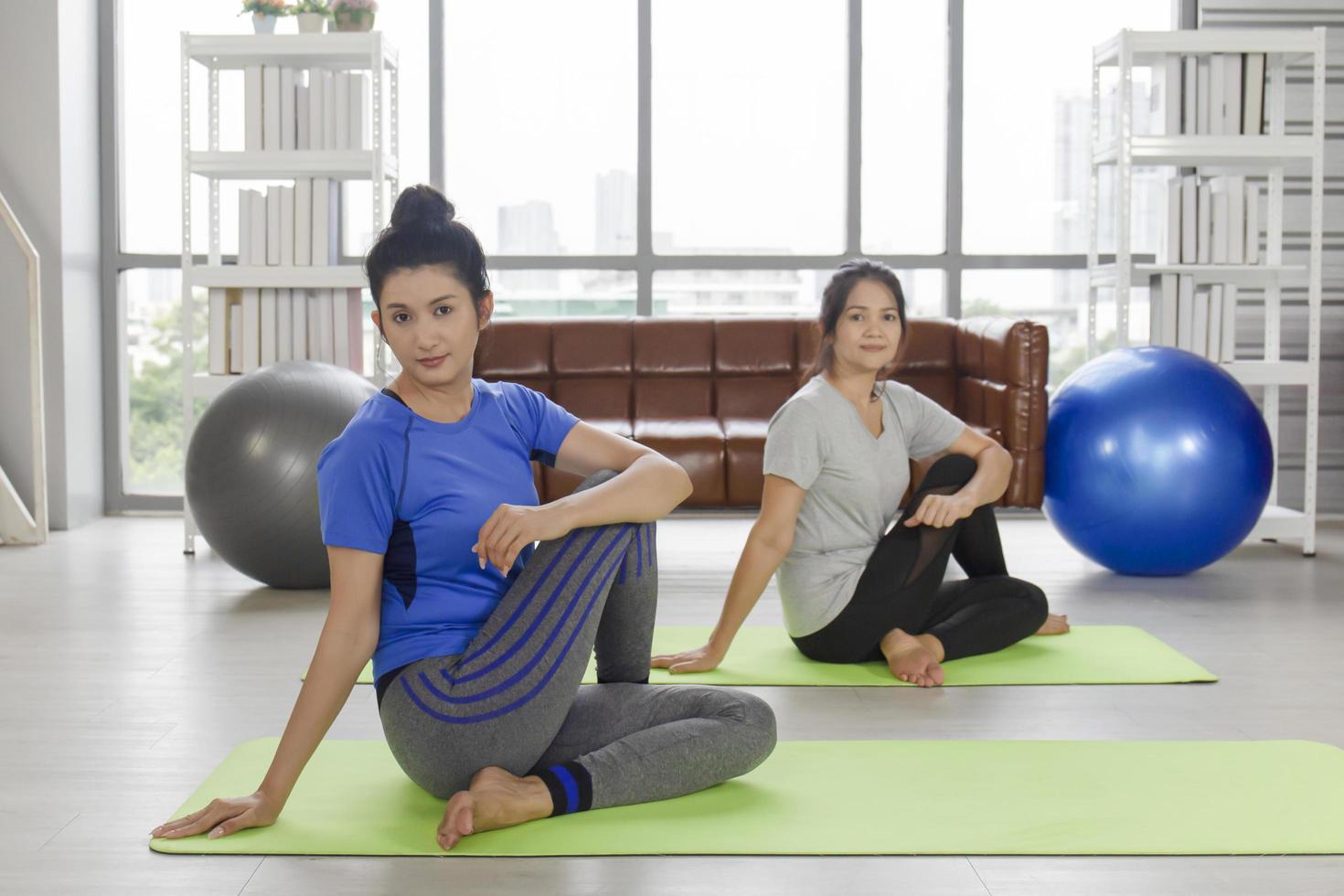 dos mujeres asiáticas de mediana edad están haciendo yoga en una alfombra de goma en su casa. foto