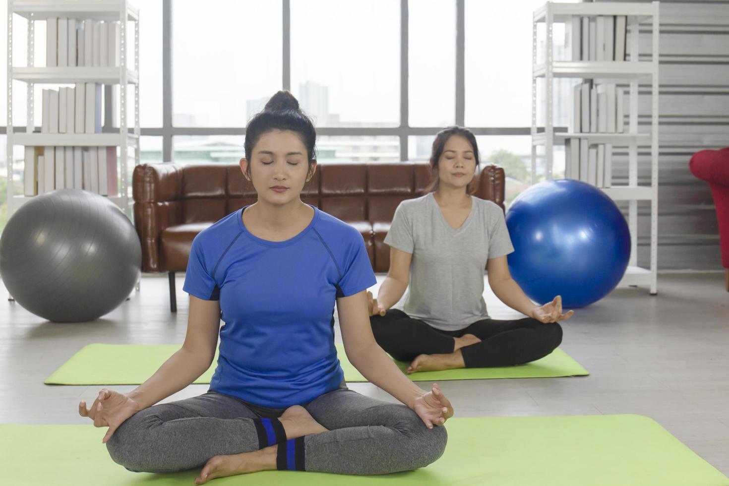 Two middle-aged Asian women are doing yoga on a rubber mat in her home. photo