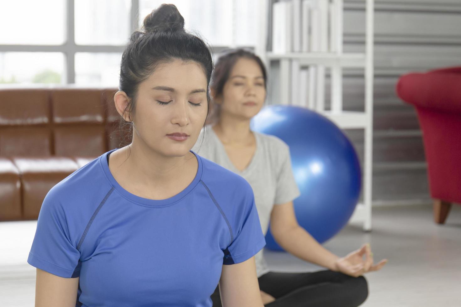 dos mujeres asiáticas de mediana edad están haciendo yoga en una alfombra de goma en su casa. foto