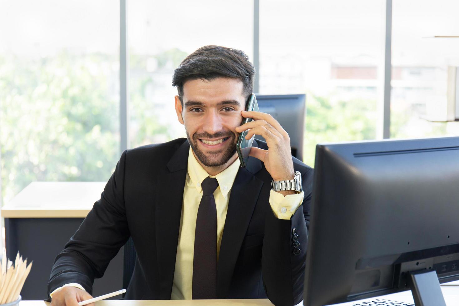 un hombre de negocios con un traje bien vestido sentado en el teléfono con una sonrisa brillante en la oficina foto