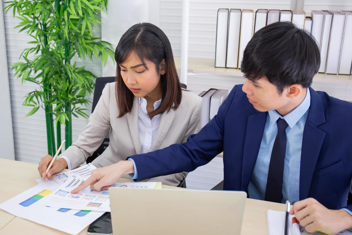 dos empleados asiáticos masculinos y femeninos ayudaron a planificar una mesa llena de documentos y tabletas, cuadernos. foto