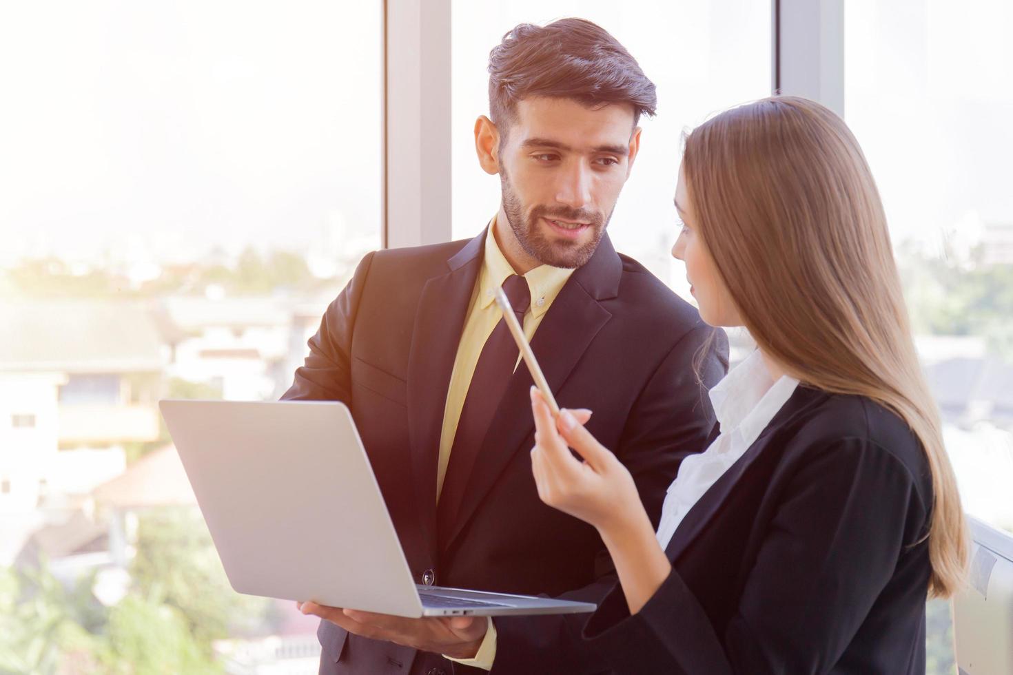 Two business men and women were neatly dressed in a suit and tie standing meeting beside the glass wall in the office. photo