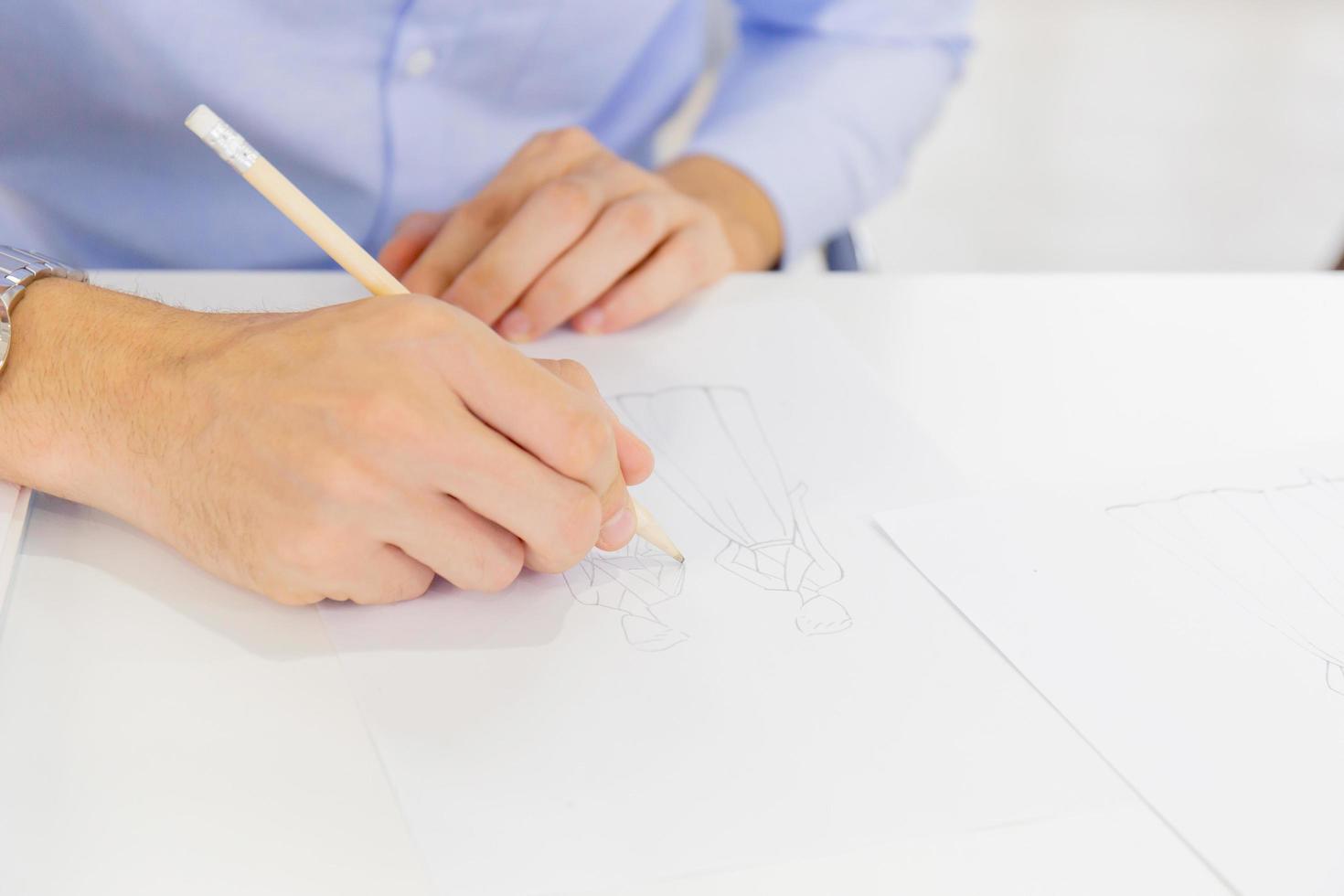 The hand of a man who is sketching on paper to design a garment photo