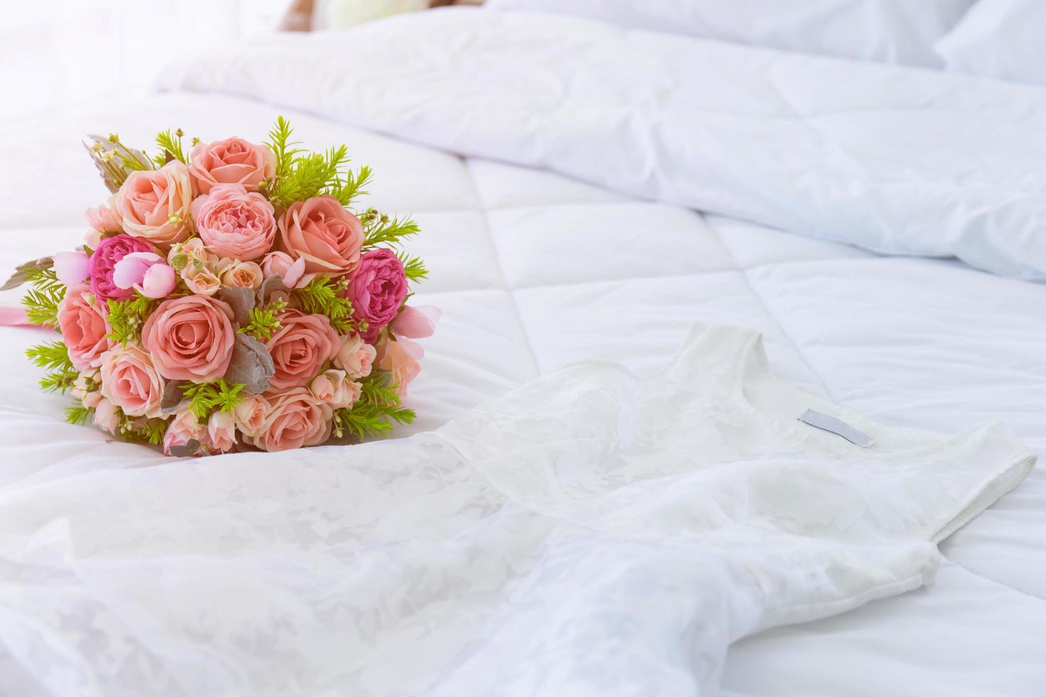 A beautiful bouquet of flowers was laid out on a clean, white bed. Next to the bridal gown were placed together. photo