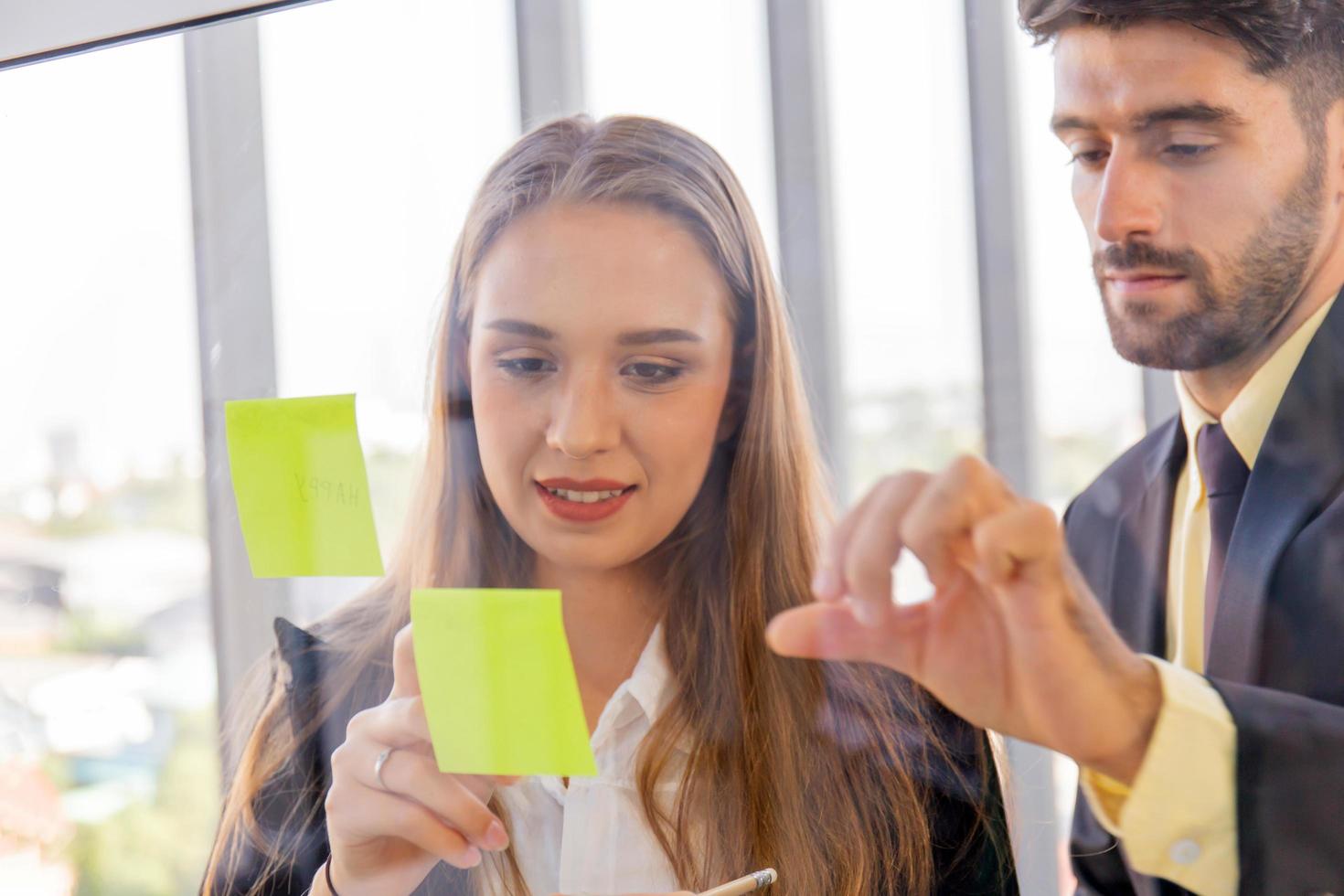 Two business men and women sticking notes on clear glass photo