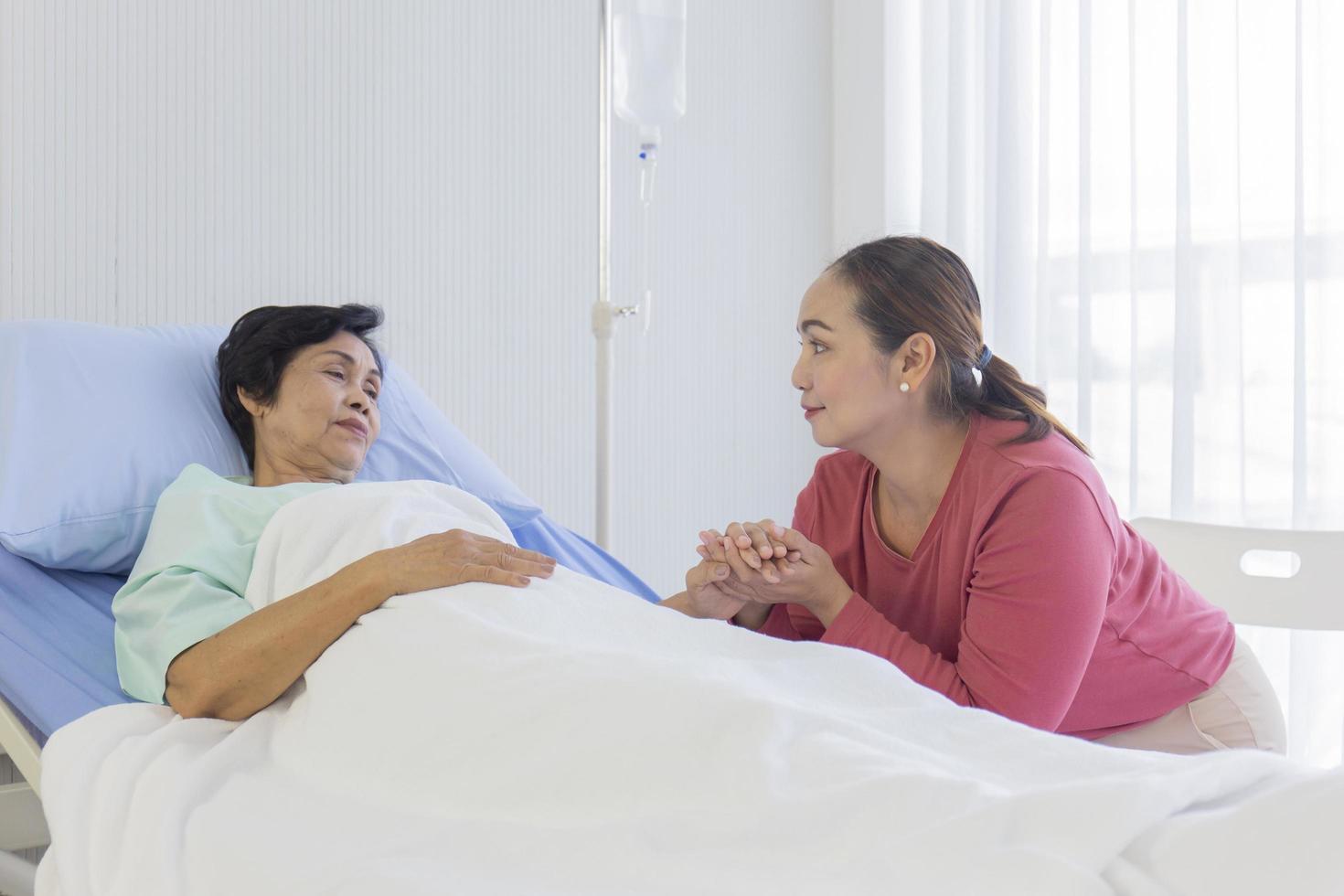 An Asian woman holds her hand to encourage her mother to sleep in a hospital bed with warmth and care. photo