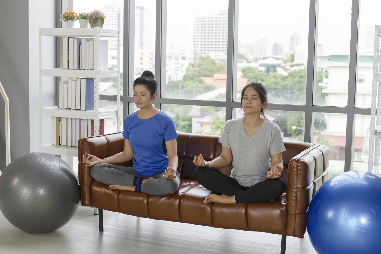 Two middle-aged Asian women do yoga on the sofa in her living room. photo