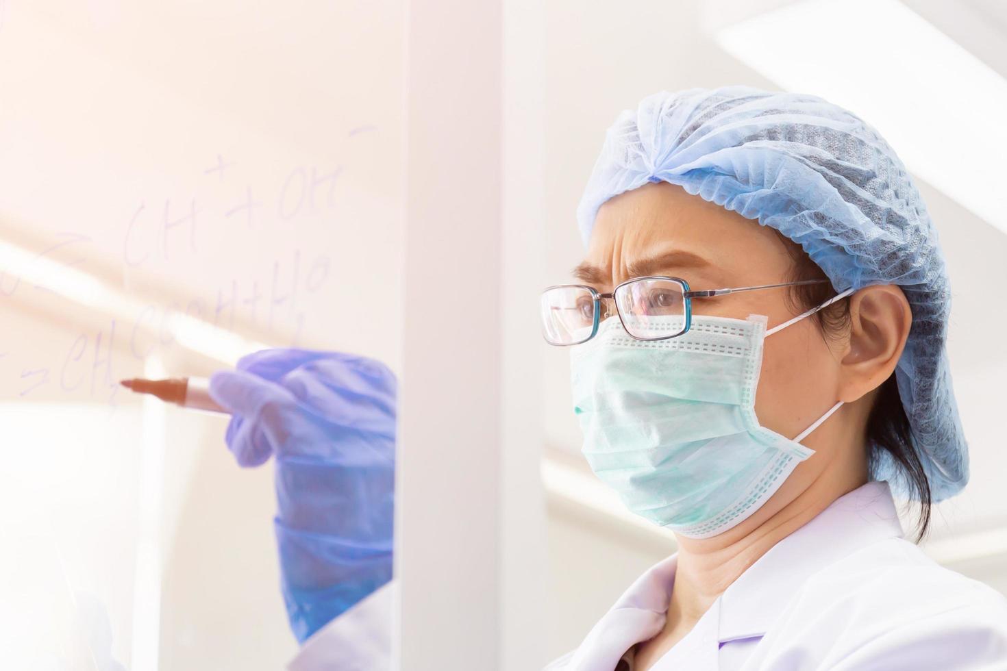 una científica asiática está escribiendo la fórmula para calcular la química en vidrio transparente en un laboratorio. foto