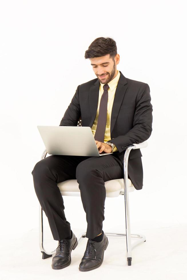 A handsome young man sitting in a chair typing on a tablet with a good mood isolated on white background, photo