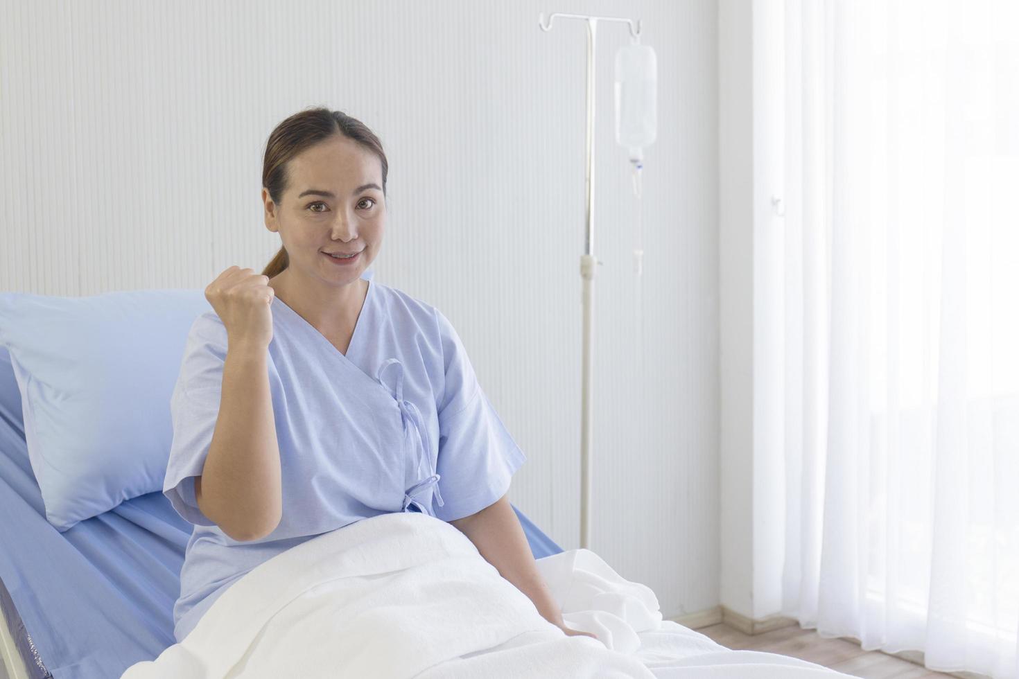 Asian female patients lie on hospital beds, raise hands, fists, show confident symptoms photo