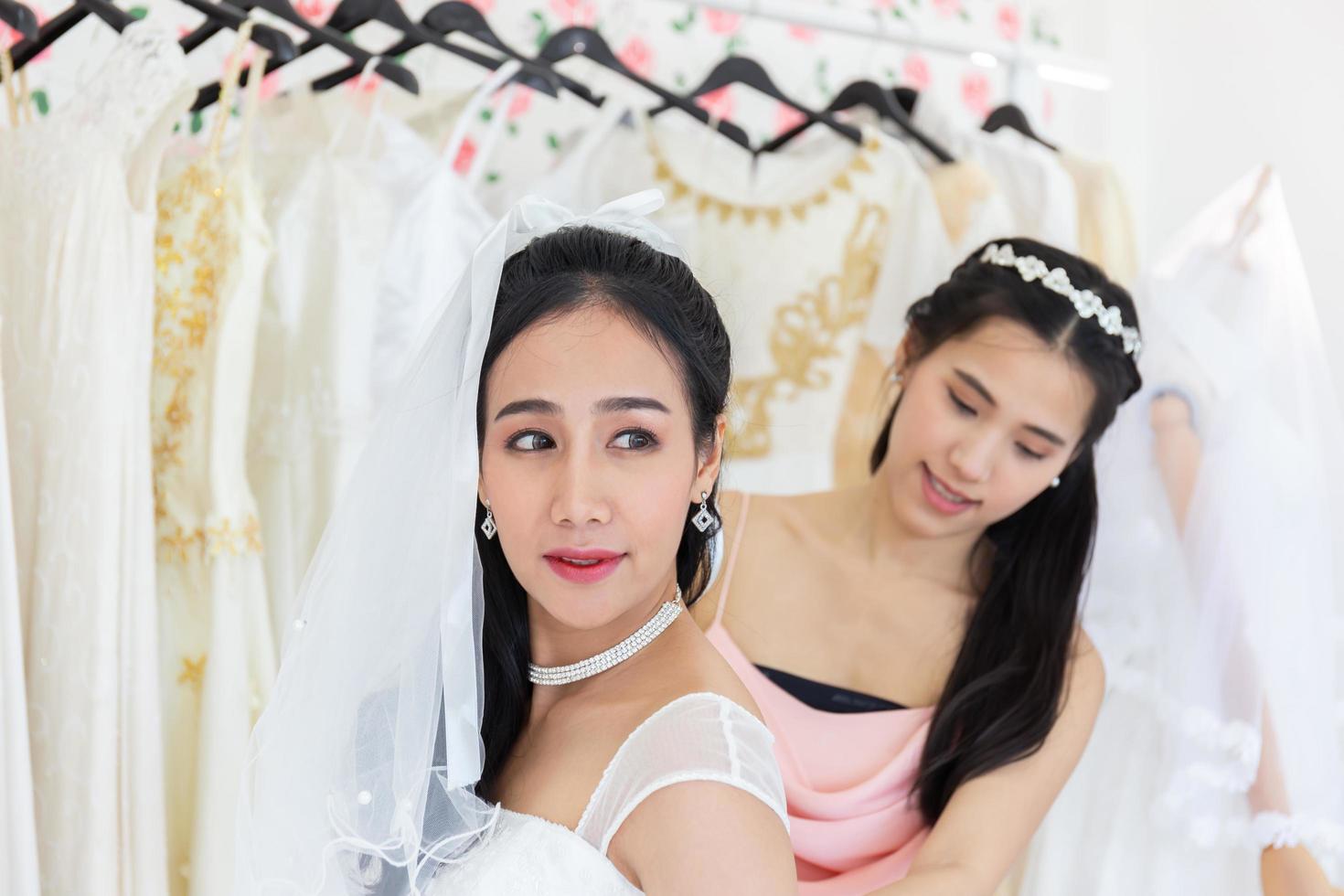 An Asian bride in a white wedding dress is trying her upcoming wedding dress in the fitting room. photo