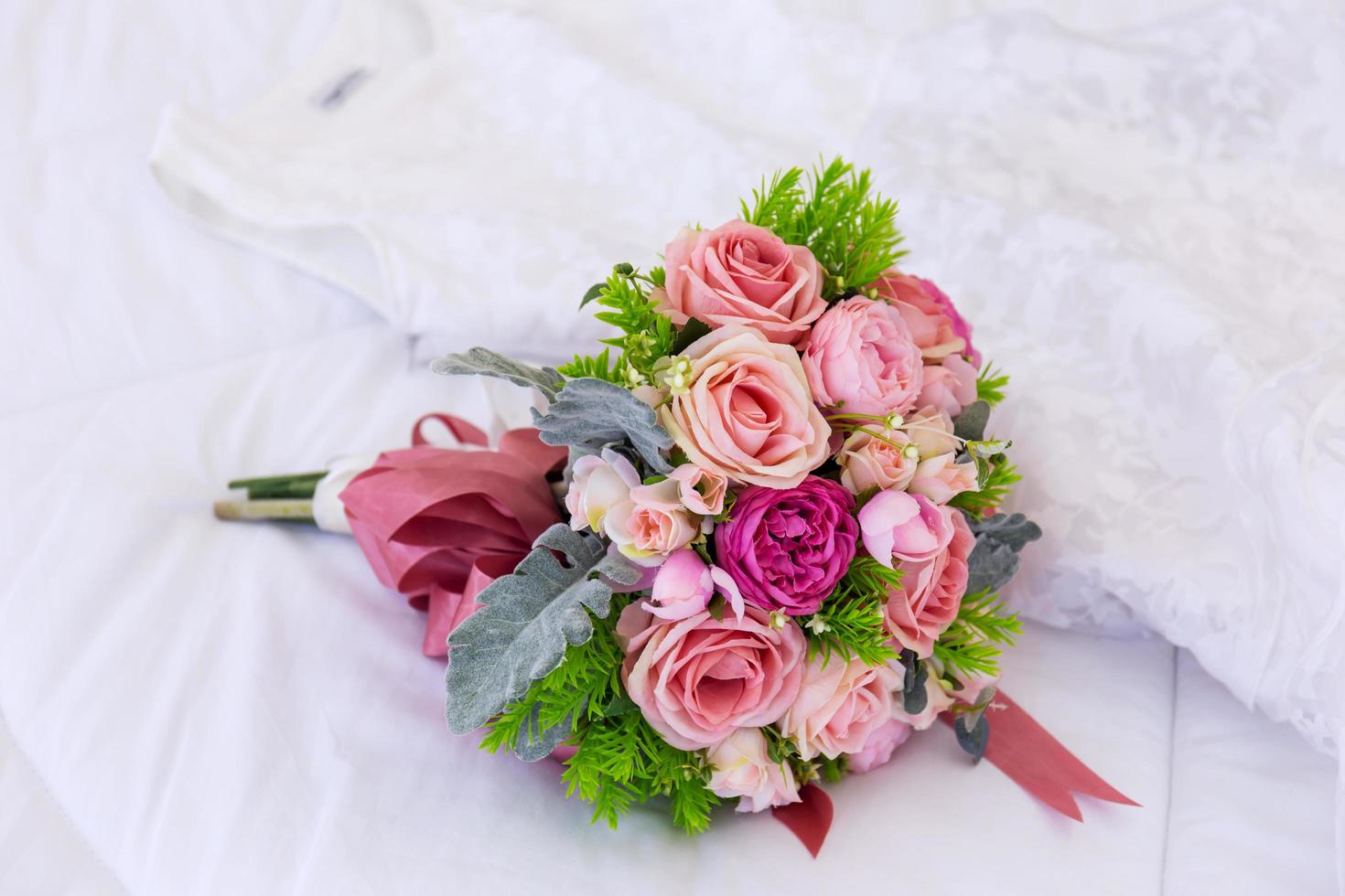 un hermoso ramo de flores estaba colocado sobre una cama limpia y blanca. junto al vestido de novia se colocaron juntos. foto