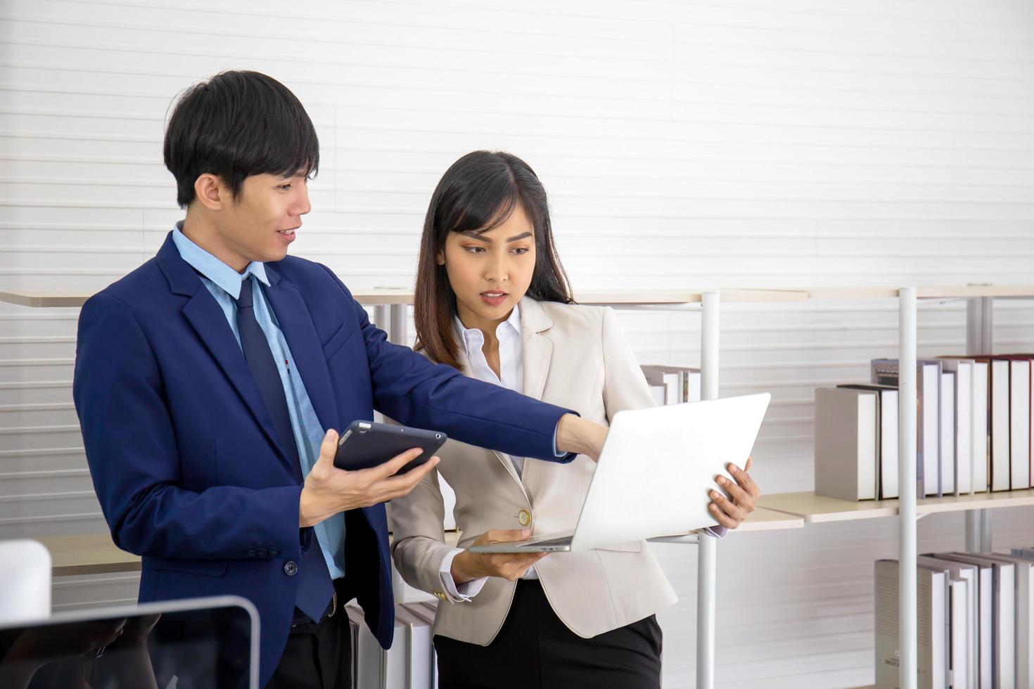 Two young Asian businessmen stand meeting in the office in the hand of the tablet. photo