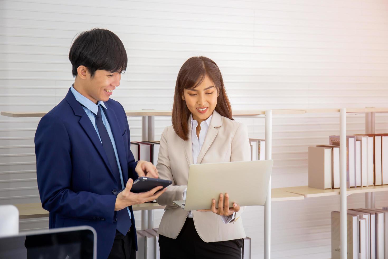 Two young Asian businessmen stand meeting in the office in the hand of the tablet. photo