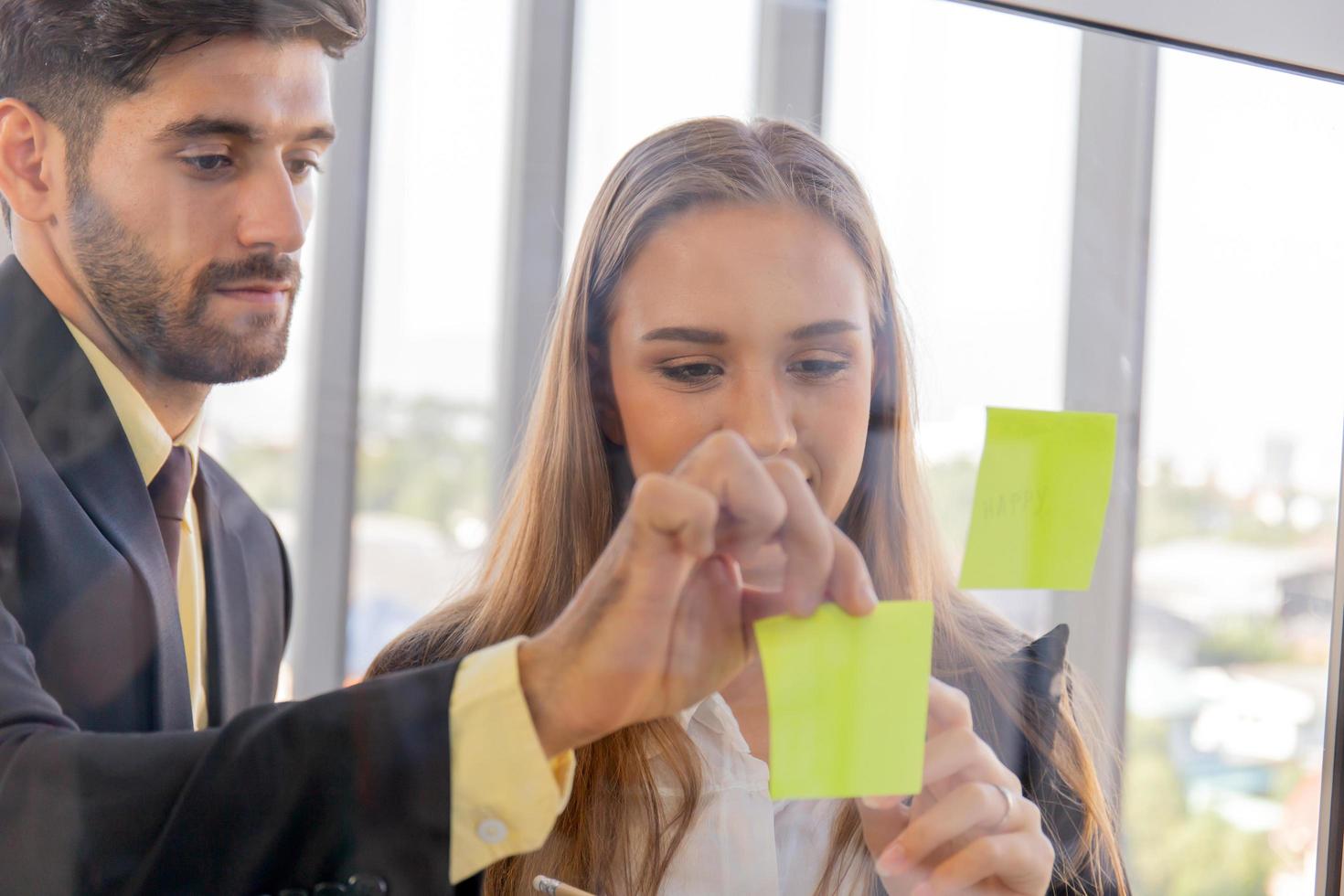 Two business men and women sticking notes on clear glass photo