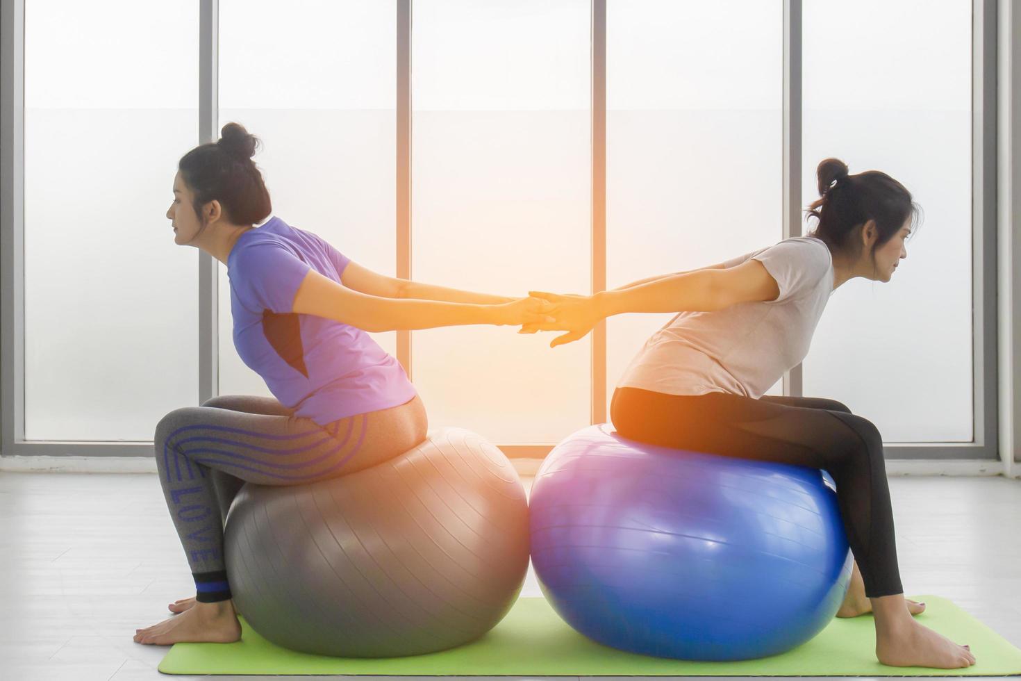 Two middle-aged Asian women doing yoga sitting on a rubber ball in the gym. photo