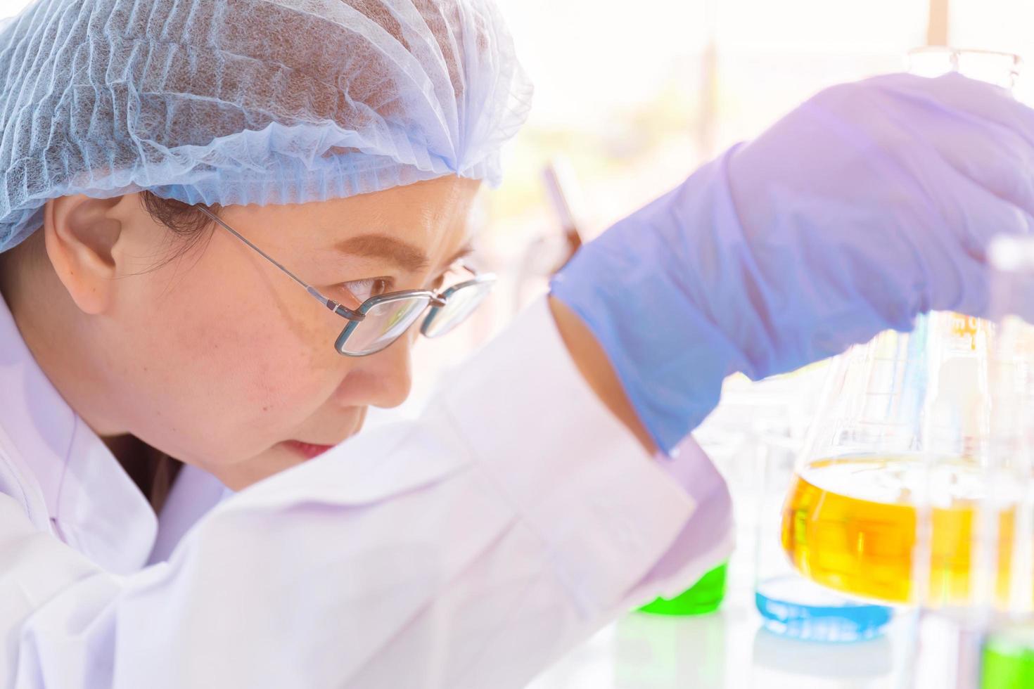 Discovering a cure for an Asian female scientist who is concentrated, holding a test tube and watching while working. photo