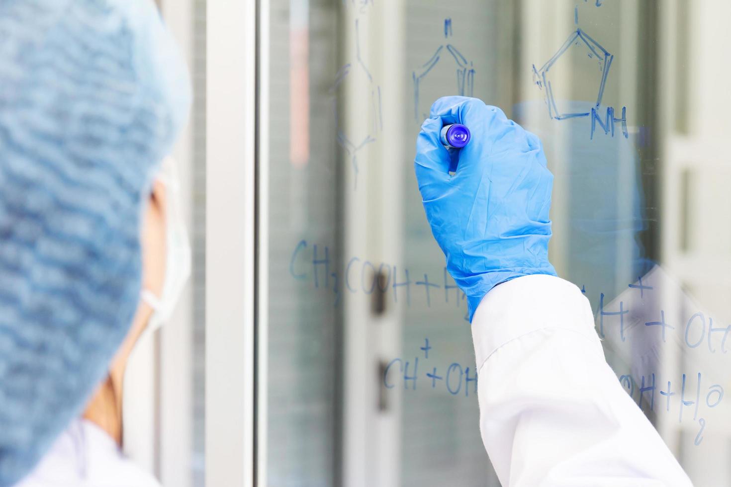 An Asian female scientist is writing down the formula for calculating chemistry on clear glass in a lab. photo