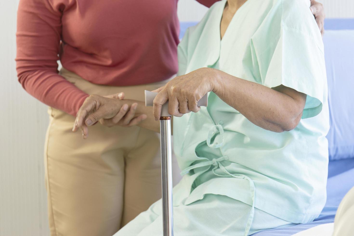 The patient's hand holding the walker helps to stand. There is a woman to take care of and support to stand. photo