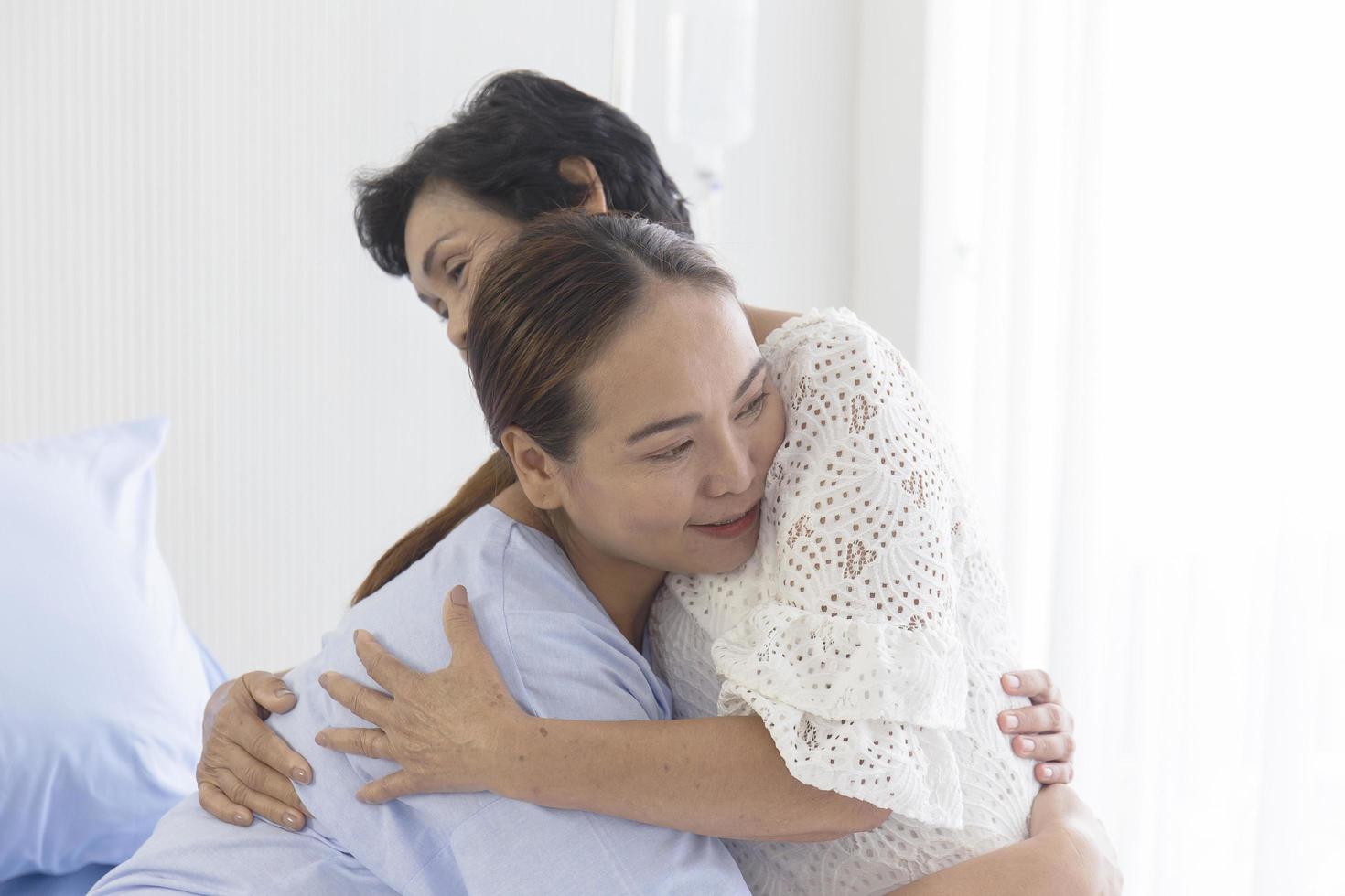 A young Asian woman who is sick in a hospital embraces her mother who looks after her. photo