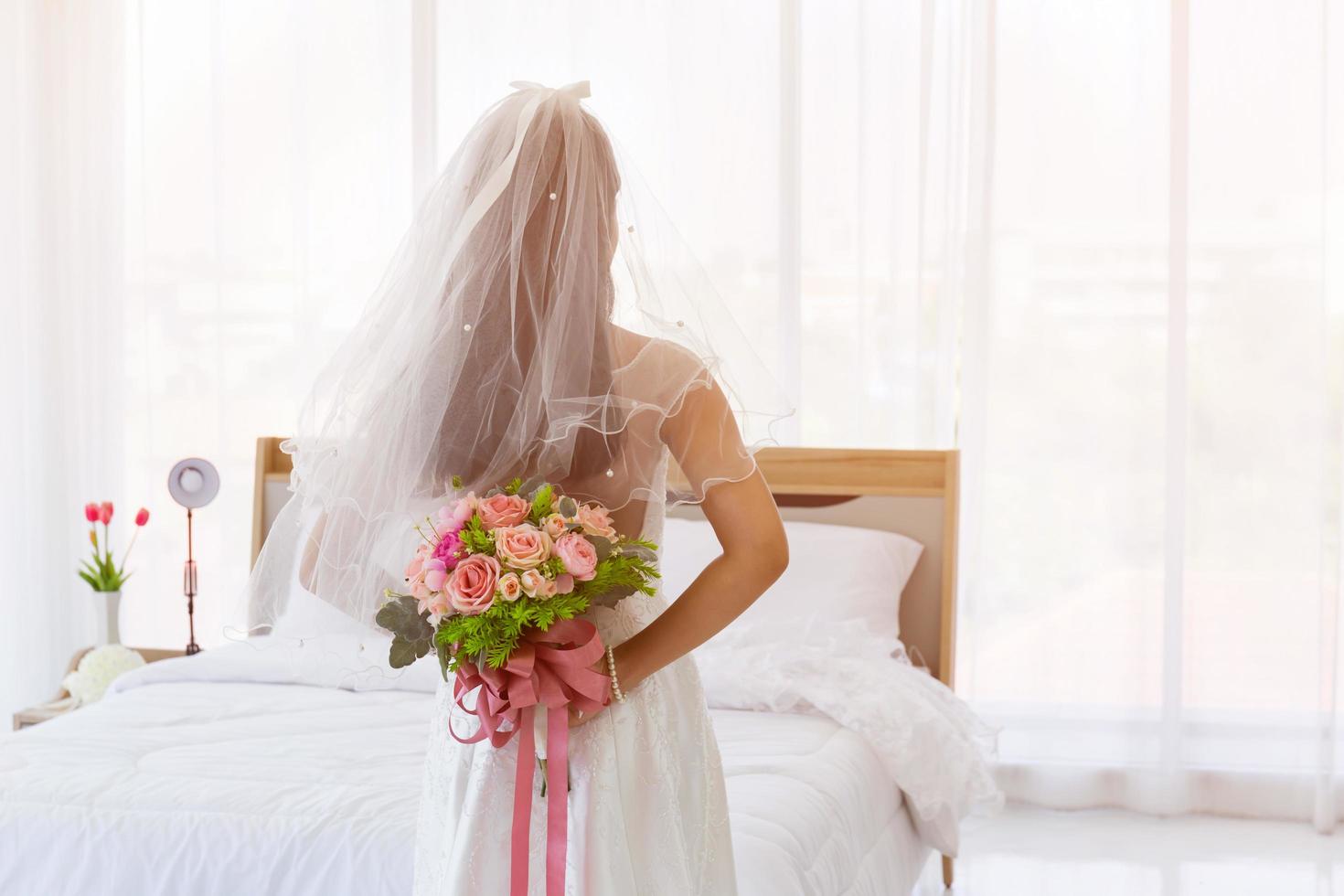 An Asian bride wore a white wedding dress, standing, holding a bouquet of beautiful flowers behind her. photo