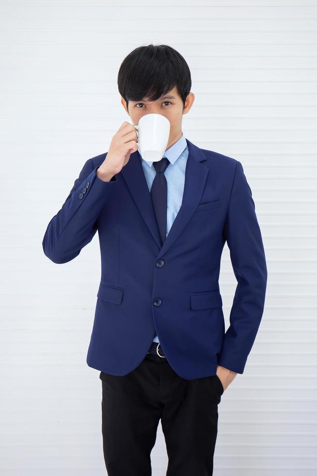 An Asian businessman stood to drink coffee and behind him was a white wall. photo