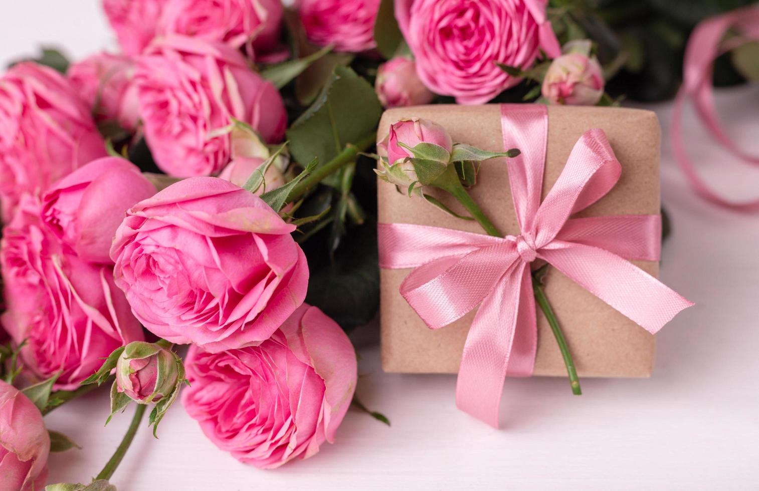 Fresh pastel soft pink roses, and gift boxes wrapped in kraft papper with ribbons on white wooden table. photo